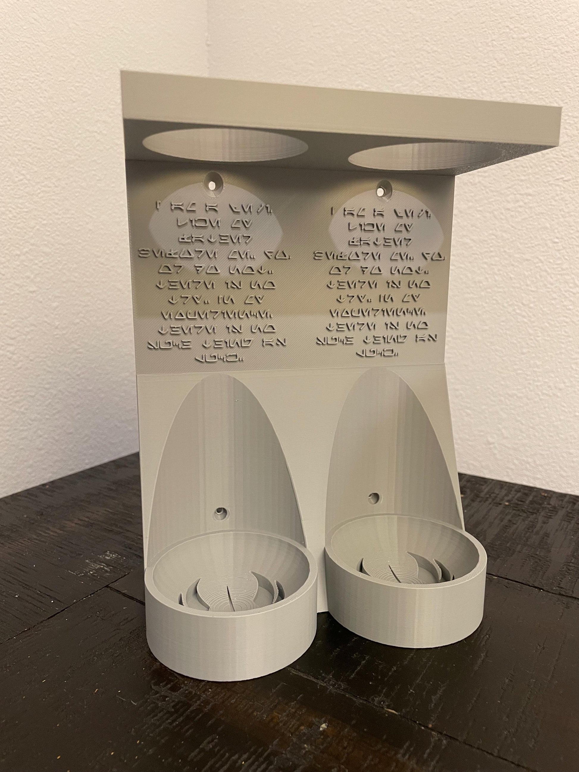 Savis Workshop Dual Lightsaber Mount shown here in the gray variant sitting on a table This vertical wall lightsaber mount is custom made to order every time. The aurebesh inscription is customizable as well as the logo in the hilt base.