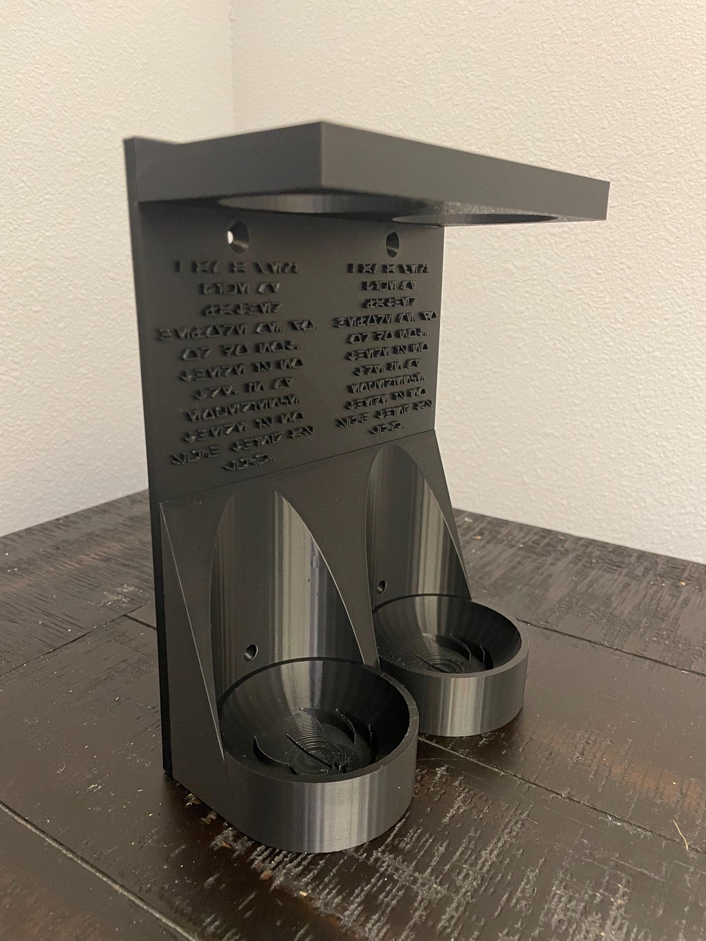 Savis Workshop Dual Lightsaber Mount shown here in the black variant sitting on a table This vertical wall lightsaber mount is custom made to order every time. The aurebesh inscription is customizable as well as the logo in the hilt base.