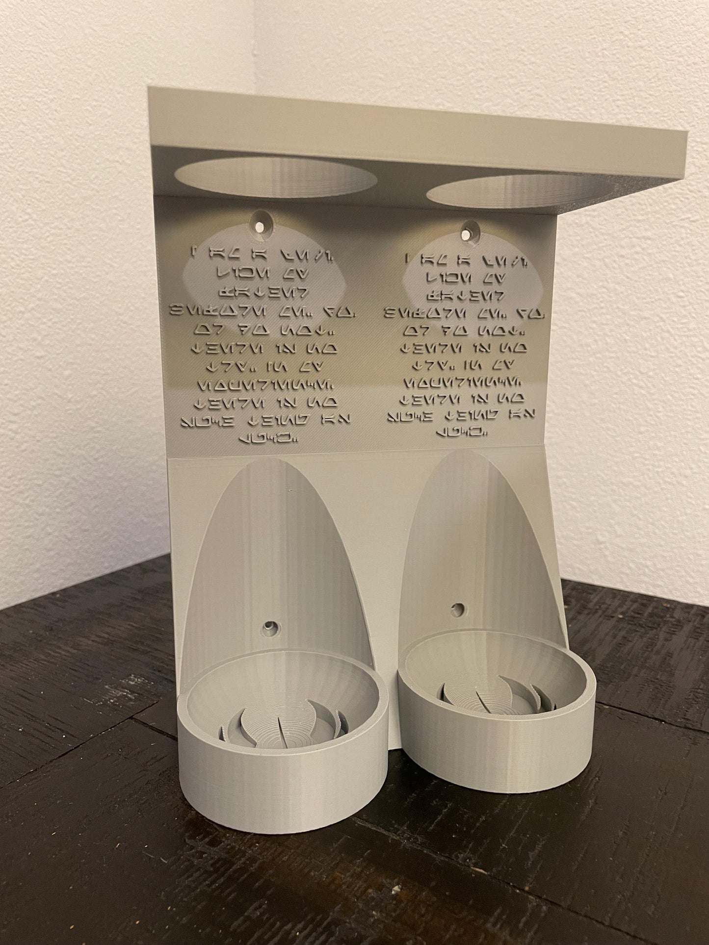 Savis Workshop Dual Lightsaber Mount shown here in the gray variant sitting on a table This vertical wall lightsaber mount is custom made to order every time. The aurebesh inscription is customizable as well as the logo in the hilt base.